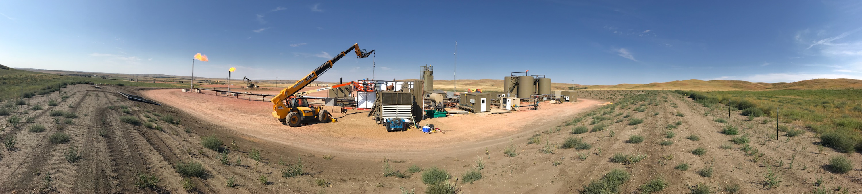 Energy infrastructure site with heavy equipment, flare stacks, and active field operations.