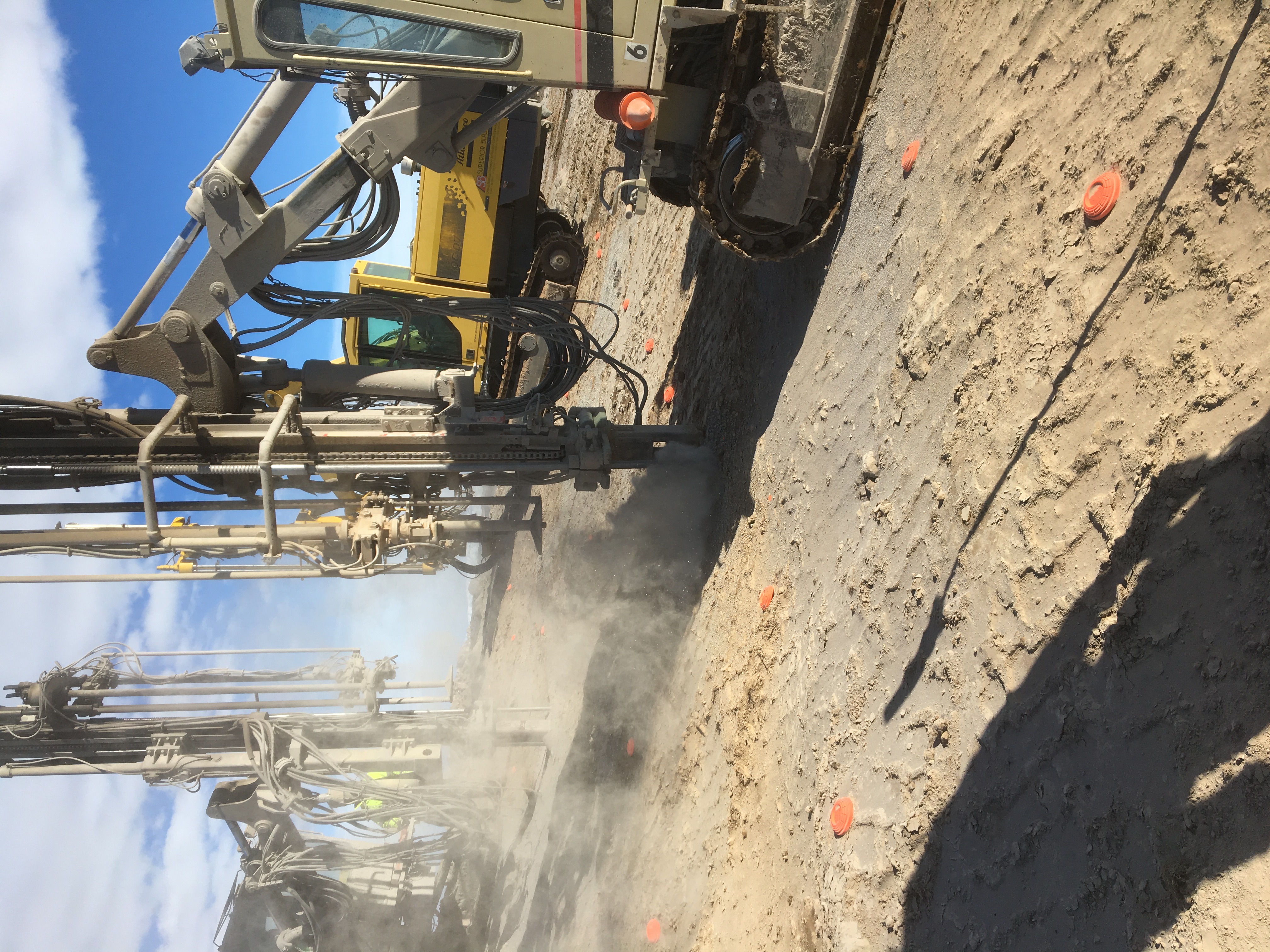 Drilling equipment in dusty field conditions under a bright sky.