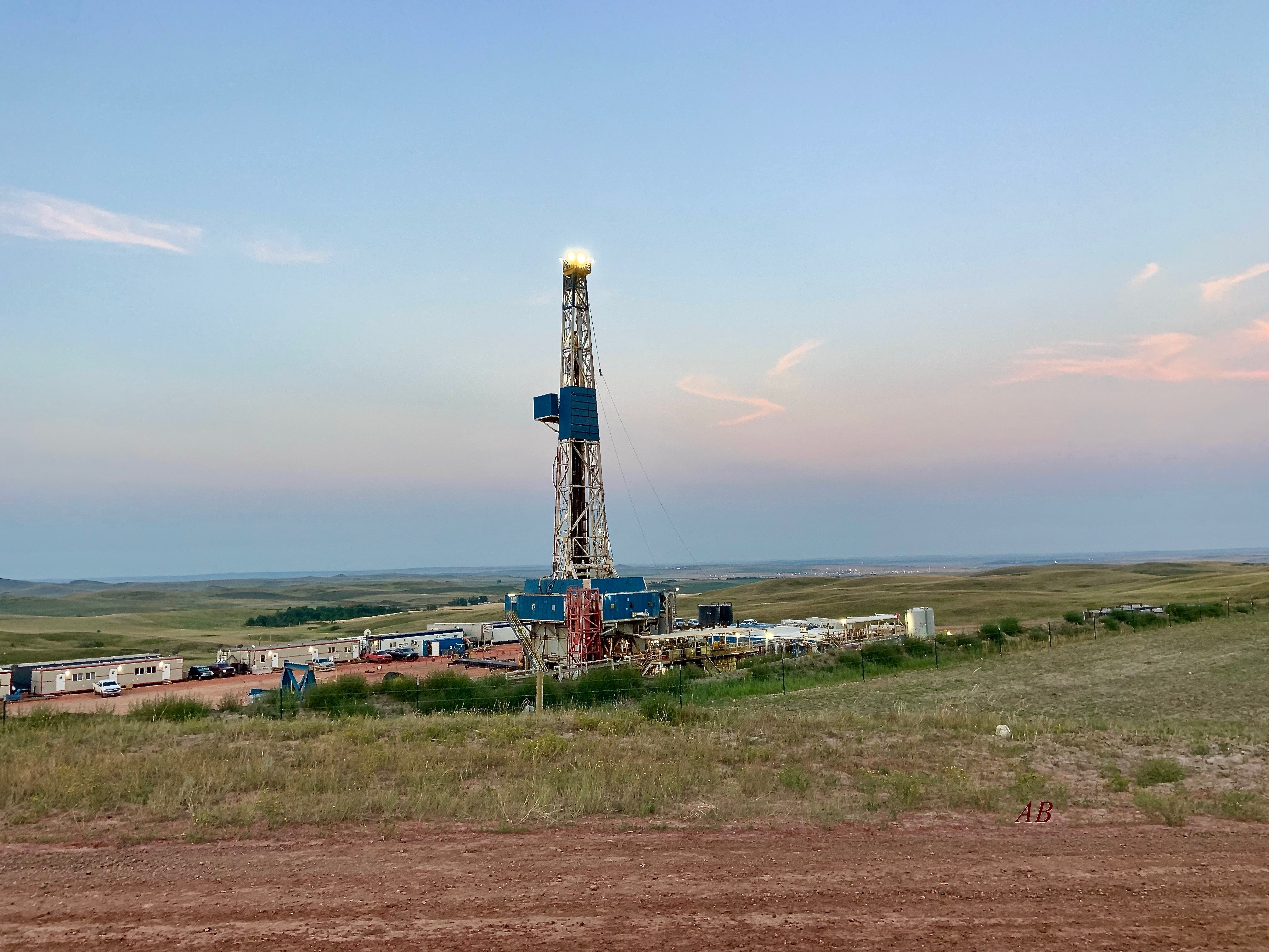 Drilling rig and surrounding field camp at dusk in an open field landscape.